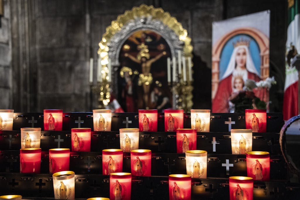 Votive candles illuminate a sacred altar in a Parisian church with religious icons and cross symbols.